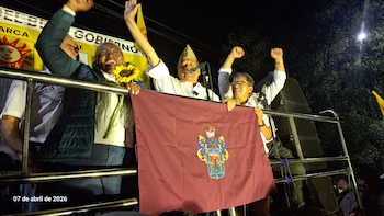 Jorge Nieto en un mitin nocturno sobre una camioneta improvisada. Sostiene un micrófono y saluda junto a otras personas sonrientes que alzan las manos y una bandera granate