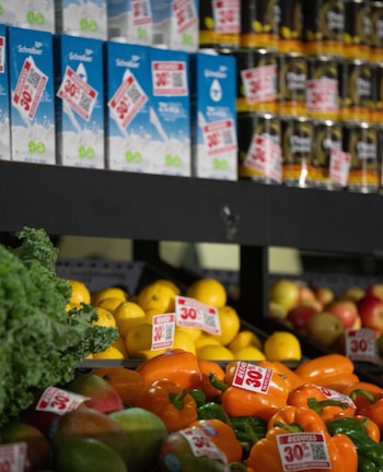 Estanterías de supermercado con cajas de leche, latas, limones, pimientos, mangos, col rizada y manzanas. Muchas etiquetas de "30% reducido" con códigos QR