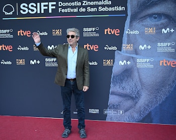 Ricardo Darín de pie sobre una alfombra roja con gafas de sol y la mano alzada frente a un panel publicitario