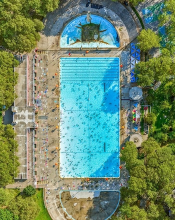 Imagen aérea cenital de la Piscina Astoria con cientos de bañistas. Se aprecian zonas de hormigón, otras piscinas vacías y árboles frondosos alrededor