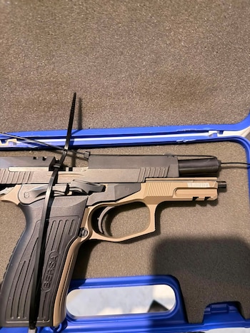 Una pistola de color negro y beige asegurada con precintos plásticos dentro de un estuche de transporte con espuma gris