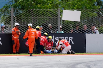 Personal médico atiende a un piloto de MotoGP, Alex Márquez, en el césped al lado de la pista tras una caída, con público detrás de una valla