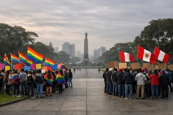 Dos grupos de personas con banderas. Grupo izquierdo con banderas arcoíris, carteles. Grupo derecho con banderas de Perú, carteles. Monumento, edificios, árboles, cielo nublado.