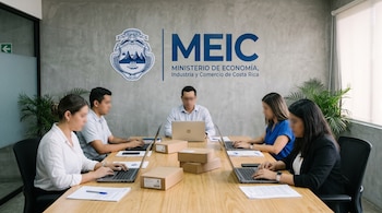 Cinco personas trabajan en laptops y con documentos en una mesa de madera. Hay cajas de cartón, plantas y el logo del MEIC con escudo de Costa Rica en la pared.