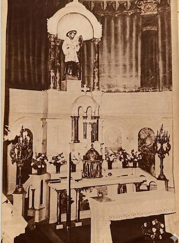 Fotografía monocromática de un altar con estatua de figura religiosa, candelabros, arreglos florales, tabernáculo y tela blanca sobre la mesa