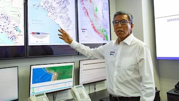 Un hombre con anteojos y camisa blanca señala un mapa del Perú proyectado en una pantalla junto a monitores con gráficos