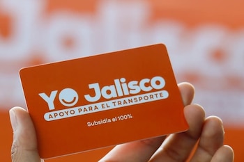 Una mano sostiene una tarjeta de plástico naranja con el texto blanco "YO Jalisco APOYO PARA EL TRANSPORTE Subsidia el 100%" y un logo de cara sonriente