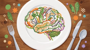 Plato blanco con cerebro ilustrado, compuesto por zanahorias, pescado, hojas verdes y lentejas. En mesa de madera, con tenedor, cuchillo, cuchara y adornos.