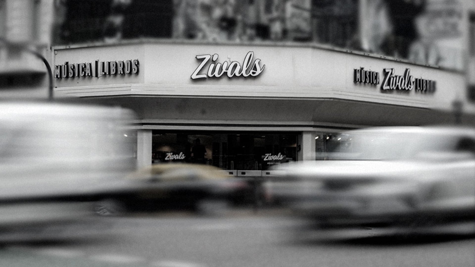 La fachada del comercio Zivals exhibe su cartelera exterior mientras varios vehículos transitan en primer plano.