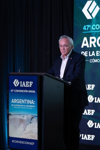 Un hombre de traje oscuro habla detrás de un atril azul con el logo de IAEF frente a una pantalla de fondo