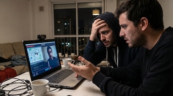 Dos hombres preocupados miran un portátil en una habitación oscura. La pantalla muestra una videollamada con un indicador "GRABANDO" y un tercer hombre.