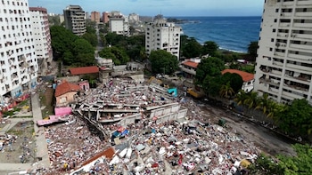 Gran pila de escombros de edificio, casas dañadas, edificios de apartamentos, personas, maquinaria de construcción, árboles, carretera y mar