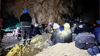 Grupo de personas con cascos sentadas y de pie dentro de una cueva o mina subterránea. El suelo es rocoso y las paredes son de piedra