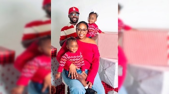 Un hombre, una mujer y dos niñas vestidas de rojo posan sonrientes rodeados de cajas de regalos con envoltorios navideños.