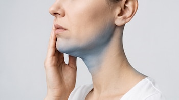 Rostro y cuello de una mujer de perfil con la mano derecha en la mandíbula, sobre un fondo gris; una sombra azul resalta la zona del cuello.
