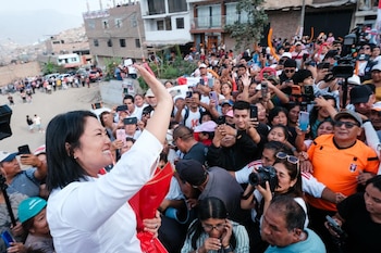 Keiko Fujimori sonríe y saluda con la mano levantada a una multitud. La gente a su alrededor la mira y graba con sus teléfonos celulares