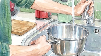 Unas manos llenan una olla de metal con agua de un grifo. Se ven azulejos verdes, una tabla de cortar y un hervidor rojo en la cocina.