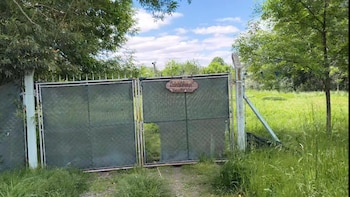 Portón metálico con malla verde y cartel de Quinta Sampi, rodeado de vegetación y árboles bajo un cielo parcialmente nublado