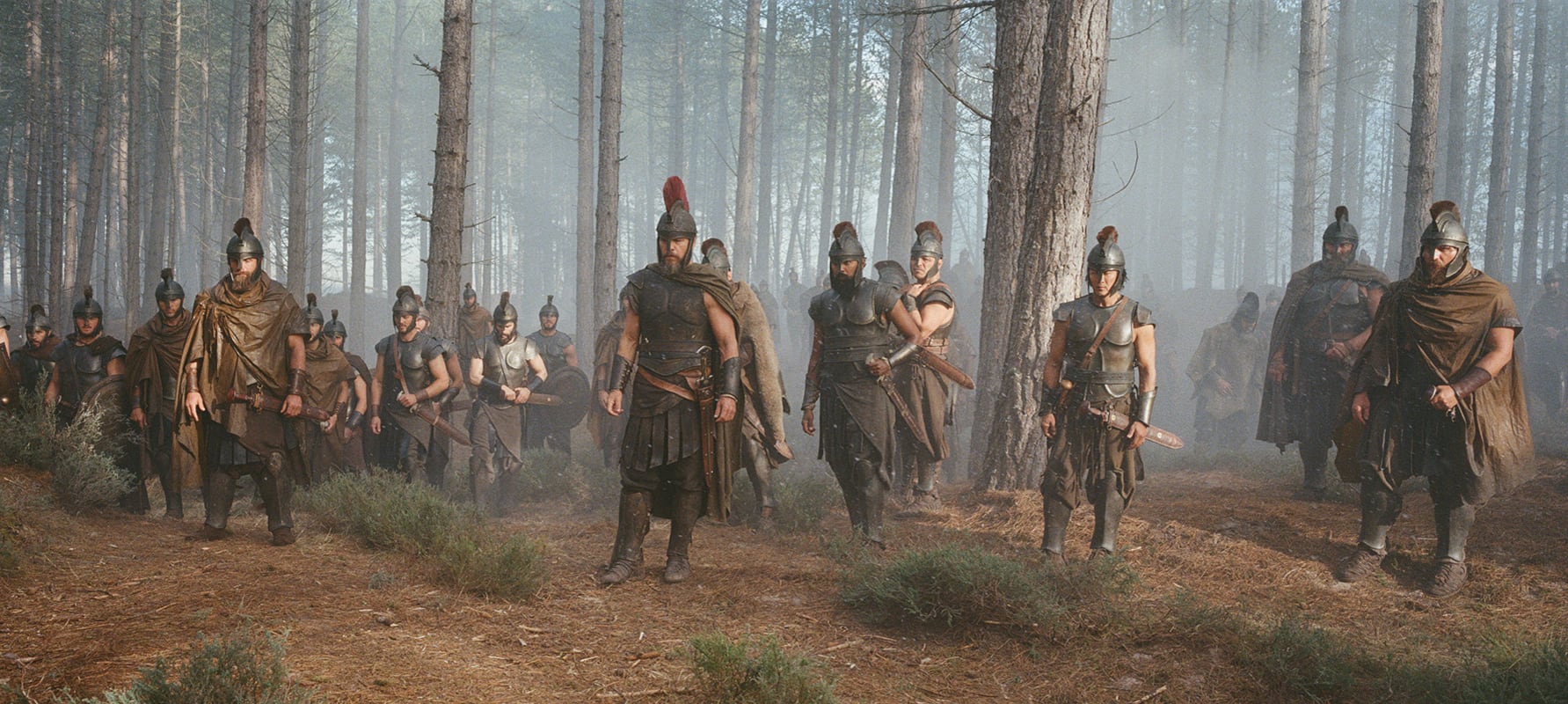 Un grupo de guerreros con cascos, armaduras y capas marcha a través de un bosque denso con árboles altos y neblina envolvente. (Foto: Universal Pictures)