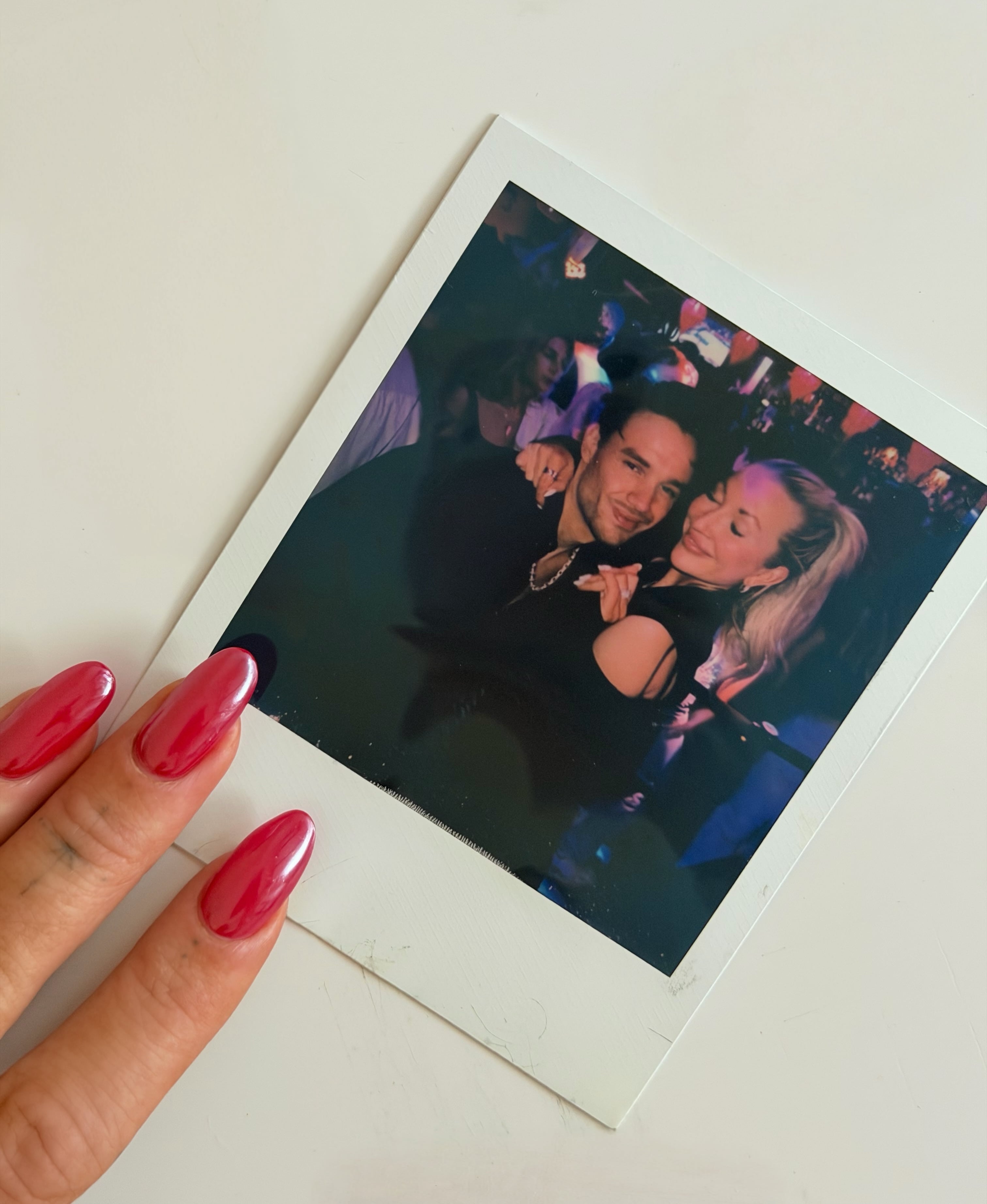 Una mano sostiene una fotografía instantánea en la que Kate Cassidy y Liam Payne posan juntos durante una celebración.