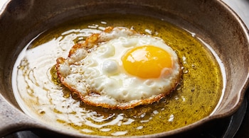 Un huevo frito con la yema intacta y la clara cuajada se cocina en una sartén con aceite burbujeante.