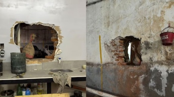 Dos boquetes visibles en paredes: uno grande en una pared blanca que da a un garaje con coches, y otro más pequeño en una pared áspera junto a un balde rojo