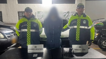 Un vehículo blanco estacionado detrás de una mesa que contiene un teléfono celular, una pistola con cargador, munición y letreros