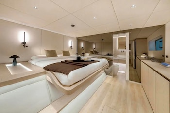 Camarote con cama doble, muebles de madera clara, apliques de luz en la pared y una puerta que comunica con un cuarto de baño