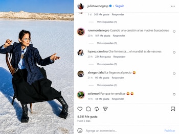 Julieta Venegas sentada en una silla de madera en un paisaje de salares bajo un cielo azul, con un blazer azul marino, pantalón negro y botas gruesas