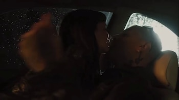 Un hombre y una mujer se acercan para besarse en los asientos delanteros de un automóvil con gotas de lluvia en la ventanilla