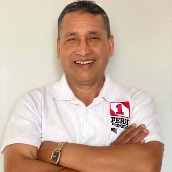 Hombre sonriente con los brazos cruzados, viste un polo blanco con el logotipo de Perú Primero y lleva un reloj dorado