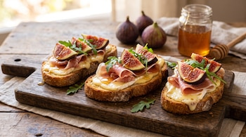 Tres tostadas con queso brie, jamón, trozos de higo y rúcula sobre una tabla de madera junto a un frasco de miel e higos enteros.