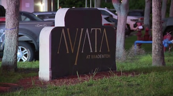 Cartel con letras doradas AVATA AT BRADENTON entre árboles, césped y coches estacionados en el fondo, con una boca de incendios roja