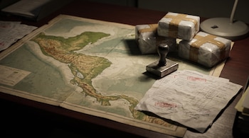 Un mapa de América Central sobre un escritorio de madera junto a un sello metálico, documentos con sellos rojos y tres paquetes embalados.