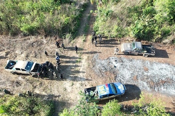 Vista aérea de un camino de tierra con varias personas y tres camionetas. Rodeado de vegetación densa y zonas de suelo quemado