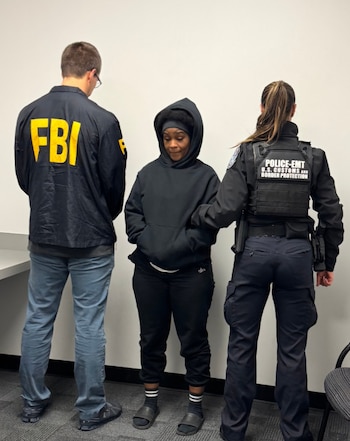 Tres personas. Agente del FBI de espaldas. Mujer con capucha negra, sujetada por agente de Aduanas y Protección Fronteriza