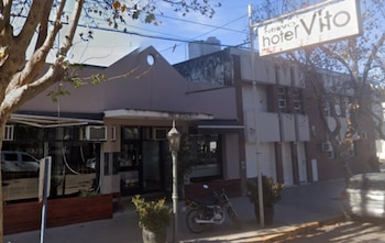 Fachada de un edificio comercial con el cartel "Nuevo hotel Vito", árboles, farola, motocicleta y automóvil estacionados en la calle
