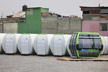 Cabina verde de AeroMetro y otras envueltas en blanco sobre grava. Al fondo, construcciones domésticas de bloques y techos de lámina con ropa tendida