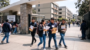 Jóvenes con sobres y credenciales caminan por la reja de entrada de una universidad junto a un letrero de admisión.