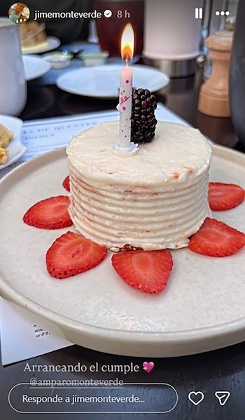 Una torta de cumpleaños de varias capas con una vela blanca encendida, una mora, y rodajas de fresas rojas alrededor, servida en un plato blanco