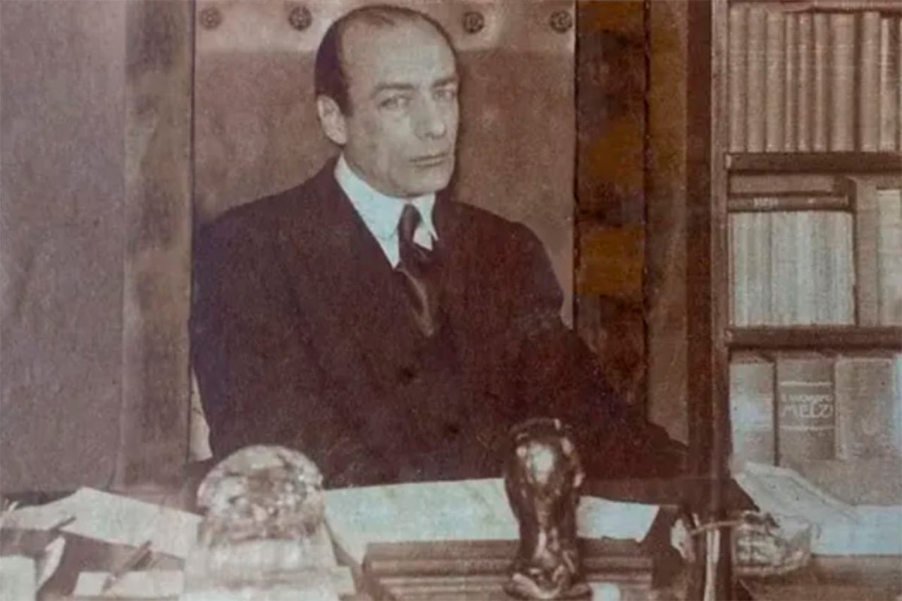 El dramaturgo y director teatral argentino Armando Discépolo permanece sentado ante su escritorio junto a un estante con libros.