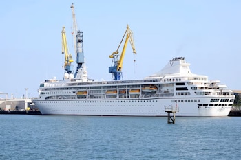 Un barco crucero blanco atracado en el muelle de un puerto junto a dos grandes grúas amarillas frente al agua