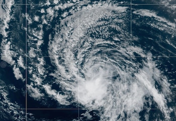 Vista satelital de una masa de nubes blancas en forma de espiral girando sobre el agua oscura del océano