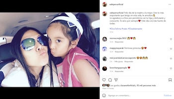 Una mujer con gafas de sol oscuras y una niña con diadema blanca posan con los labios fruncidos en un coche, tomándose una selfie