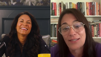 Dos mujeres en una videollamada; la de la izquierda sonríe, y la de la derecha usa gafas frente a una estantería de libros