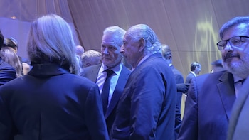 Personas vestidas con traje formal conversan de pie en un salón interior iluminado por luces de tono azulado