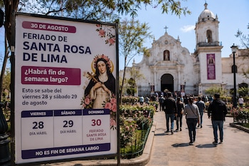 Cartel informativo sobre el feriado del 30 de agosto junto a personas caminando por una plaza frente a una iglesia blanca
