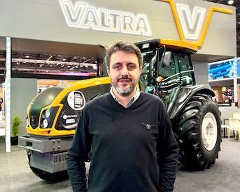 Hombre de barba posa frente a tractor Valtra amarillo y negro. Al fondo, un letrero con la marca Valtra V y parte de otra maquinaria