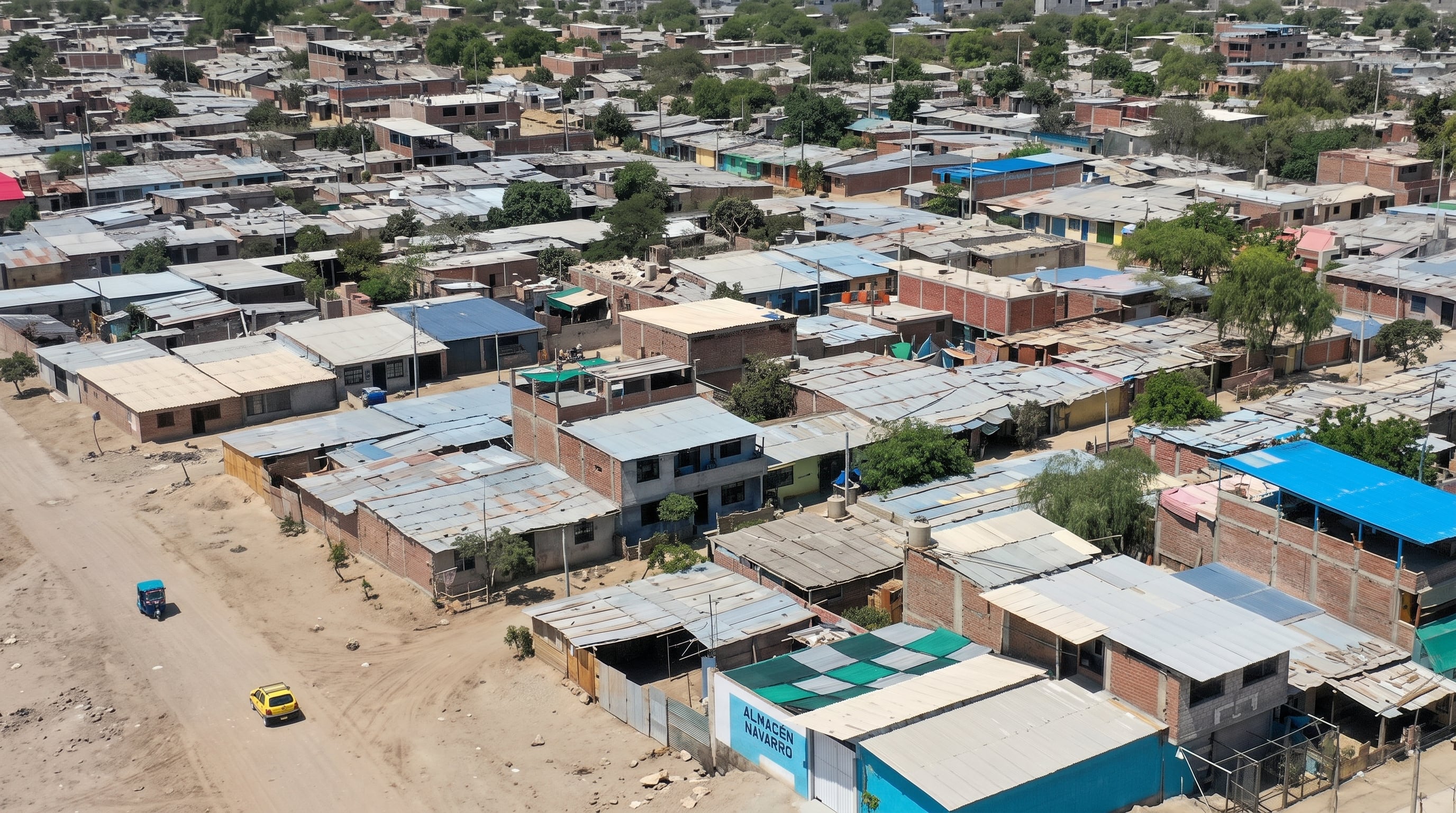 Un conjunto de viviendas de ladrillo y techos metálicos se extiende junto a una calle de tierra transitada por vehículos menores.