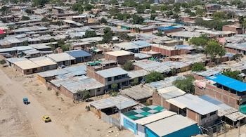 Vista elevada de casas con techos metálicos y de ladrillo junto a una calle de tierra donde transitan un mototaxi y un automóvil amarillo.